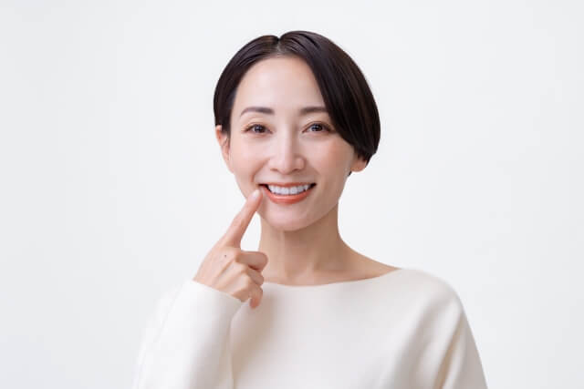 口元を指さして微笑む女性